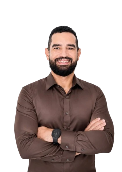 Professor Pedro Júnior, sorrindo, de camisa marrom e braços cruzados.